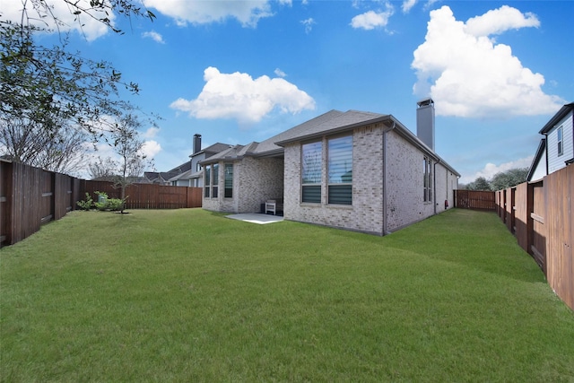 rear view of property with a chimney, a yard, brick siding, and a fenced backyard