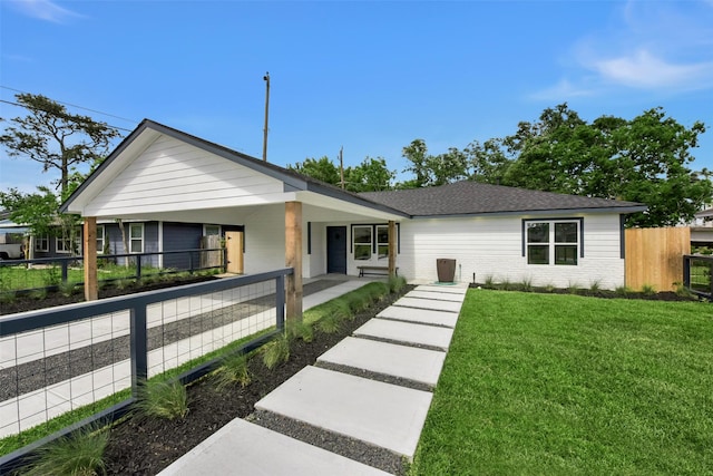 ranch-style home featuring covered porch, fence, brick siding, a front lawn, and a shingled roof