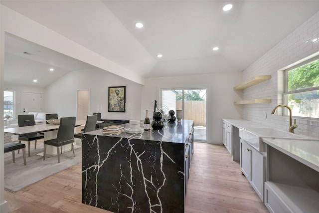 kitchen with light wood-type flooring, plenty of natural light, vaulted ceiling, and a sink