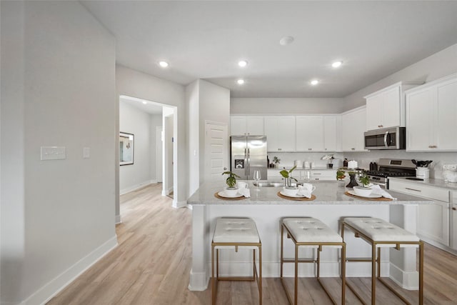 kitchen featuring a breakfast bar, stainless steel appliances, white cabinets, and light wood-type flooring
