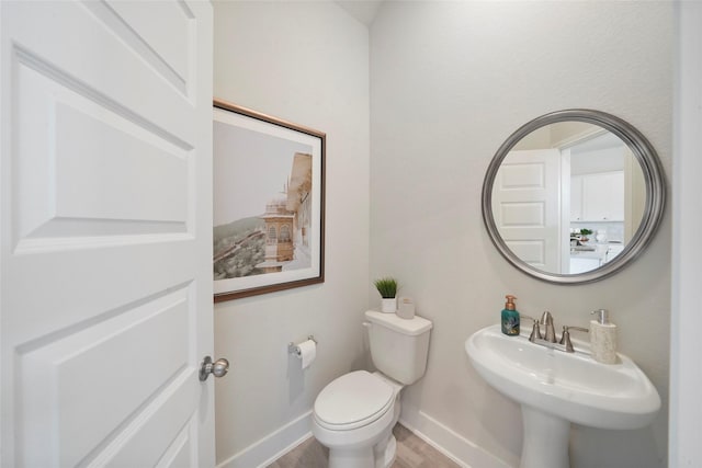 half bathroom with toilet, baseboards, a sink, and wood finished floors