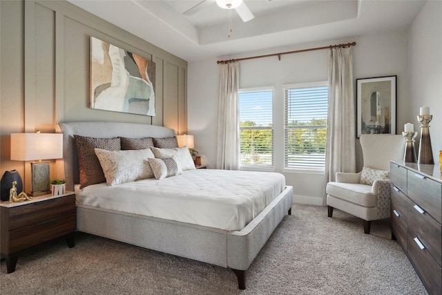 bedroom with a tray ceiling, light carpet, baseboards, and ceiling fan