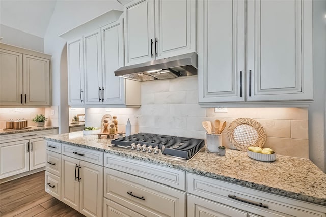 11131 Heartleaf Aster Way, Cypress, TX 77433 - kitchen with wood finished floors, stainless steel gas stovetop, light stone counters, under cabinet range hood, and backsplash