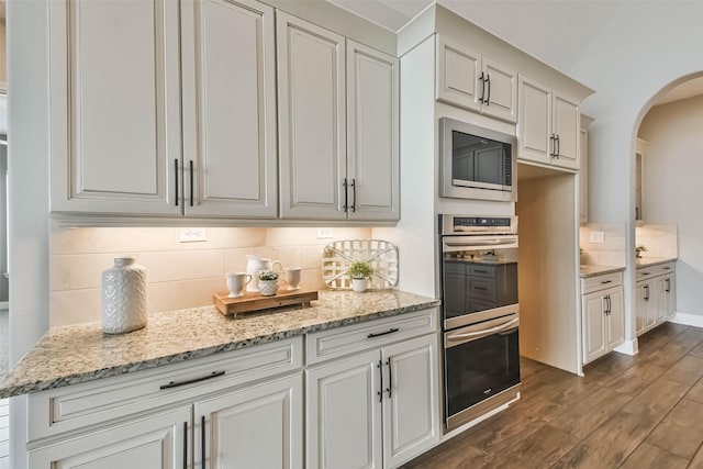 11131 Heartleaf Aster Way, Cypress, TX 77433 - kitchen with built in microwave, stainless steel double oven, arched walkways, backsplash, and dark wood-style floors