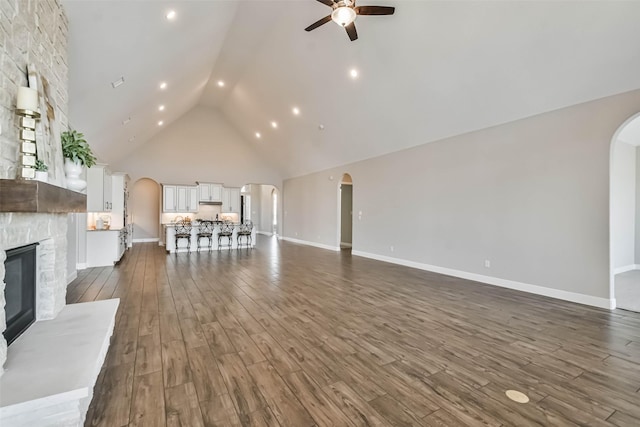 11131 Heartleaf Aster Way, Cypress, TX 77433 - unfurnished living room with high vaulted ceiling, ceiling fan, a stone fireplace, arched walkways, and dark wood-style floors