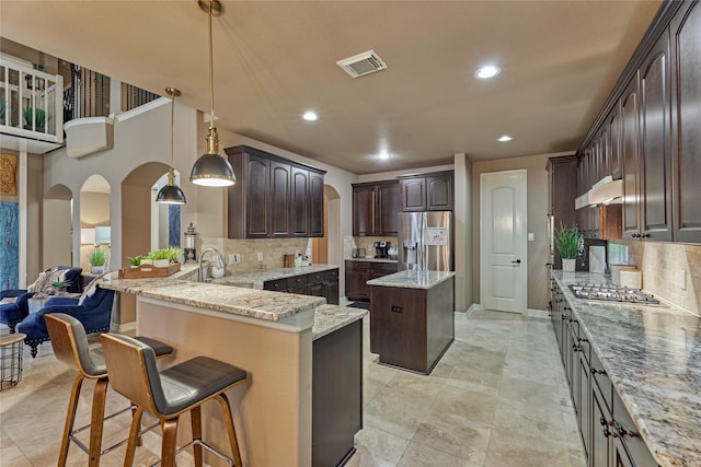 19089 Grandview Pt, Montgomery, TX 77356 - kitchen with appliances with stainless steel finishes, under cabinet range hood, arched walkways, dark brown cabinets, and backsplash