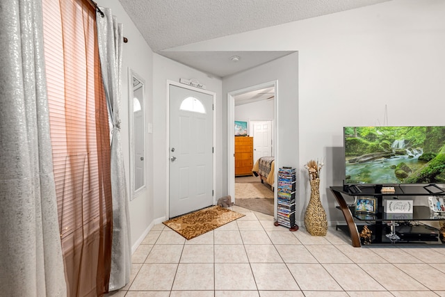 foyer featuring light tile patterned floors, baseboards, a textured ceiling, and vaulted ceiling