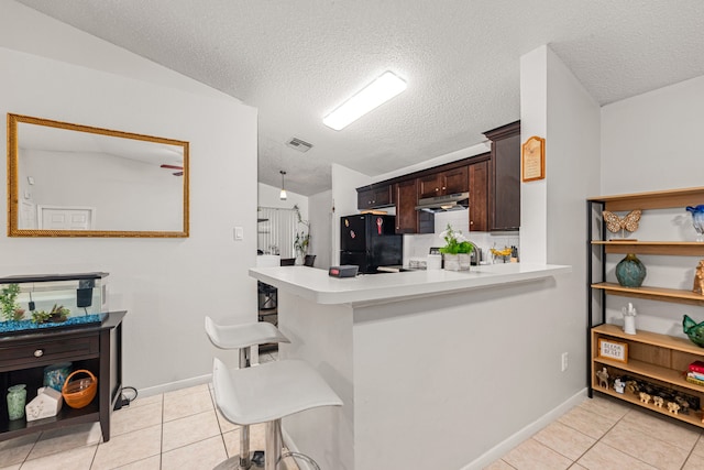 kitchen featuring a breakfast bar, freestanding refrigerator, light countertops, and light tile patterned floors