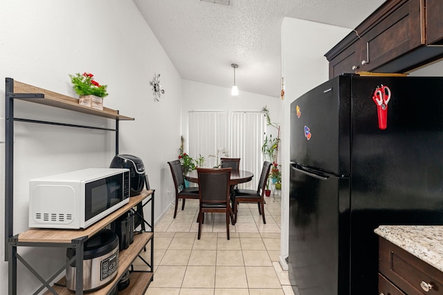 kitchen featuring white microwave, freestanding refrigerator, lofted ceiling, and dark brown cabinetry