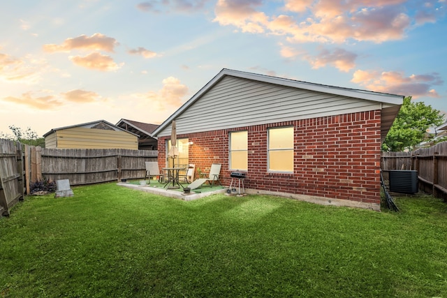 back of house with brick siding, a patio, a fenced backyard, a lawn, and central AC unit