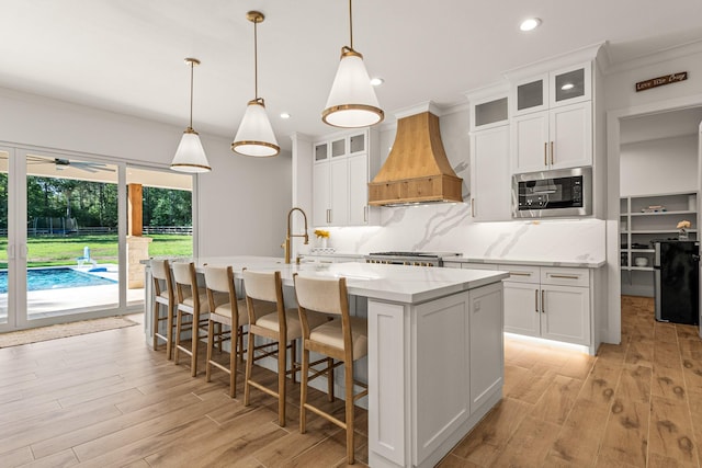 8577 Majestic Lake Ct, Montgomery, TX 77316 - kitchen featuring custom range hood, stainless steel microwave, an island with sink, light wood-style flooring, and recessed lighting