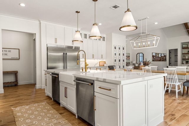 8577 Majestic Lake Ct, Montgomery, TX 77316 - kitchen with stainless steel appliances, a center island with sink, light wood finished floors, white cabinetry, and light stone counters
