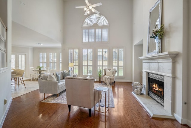 living room with a tile fireplace, a ceiling fan, a towering ceiling, wood finished floors, and baseboards