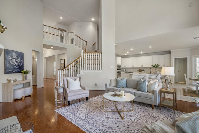 living area featuring a towering ceiling, stairs, baseboards, wood finished floors, and recessed lighting