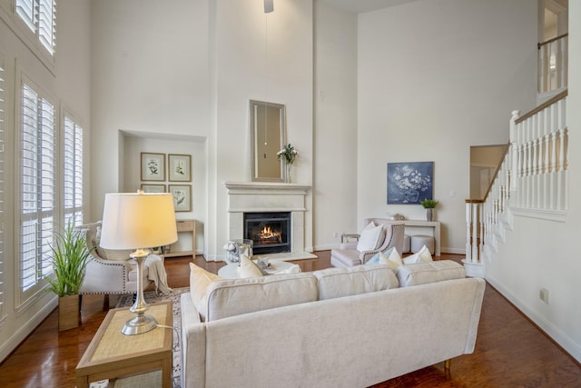 living room with a high ceiling, a glass covered fireplace, baseboards, stairs, and dark wood-style flooring