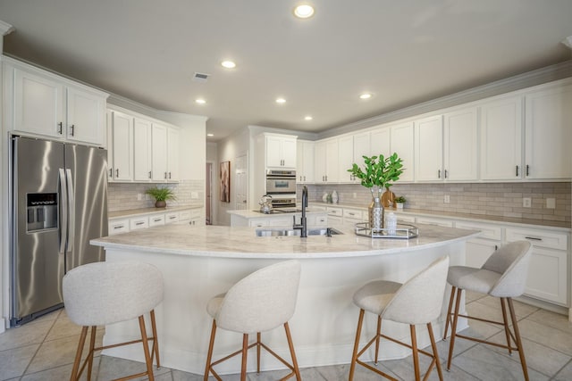 kitchen with stainless steel fridge with ice dispenser, a center island with sink, a sink, tasteful backsplash, and white cabinetry