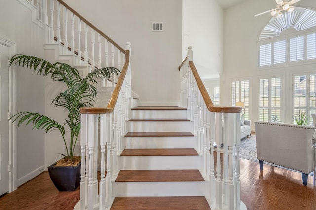 stairs featuring wood finished floors, a ceiling fan, and a towering ceiling