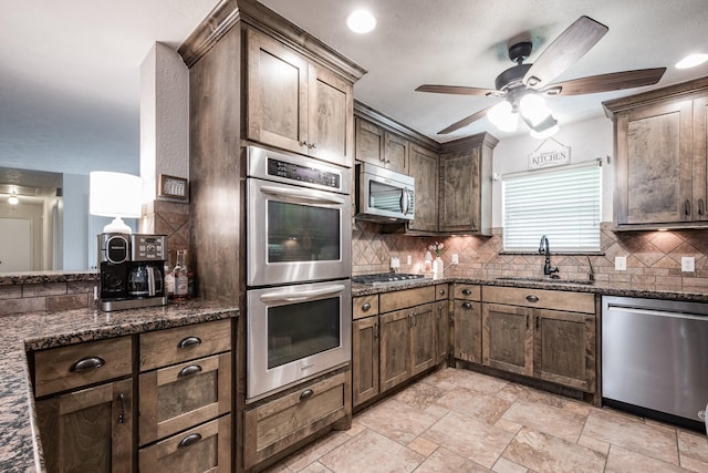 kitchen with a ceiling fan, dark stone countertops, a sink, stainless steel appliances, and tasteful backsplash