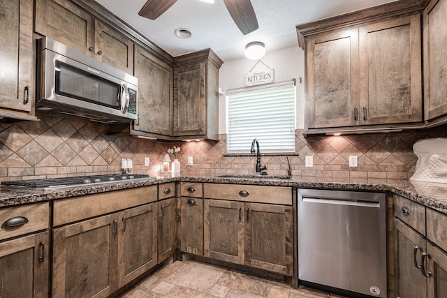 kitchen with ceiling fan, a sink, backsplash, stainless steel appliances, and dark stone counters