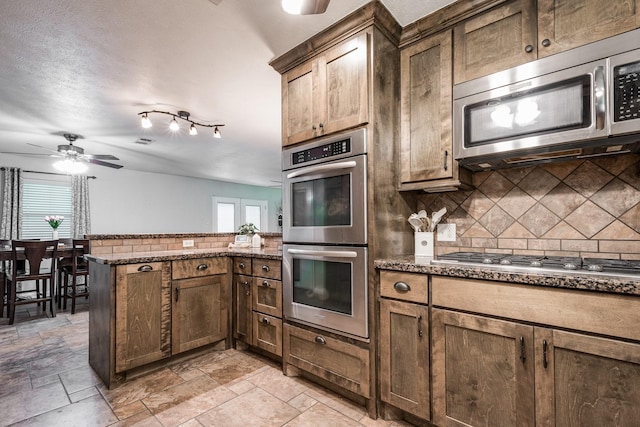 kitchen with backsplash, a peninsula, appliances with stainless steel finishes, and dark stone counters