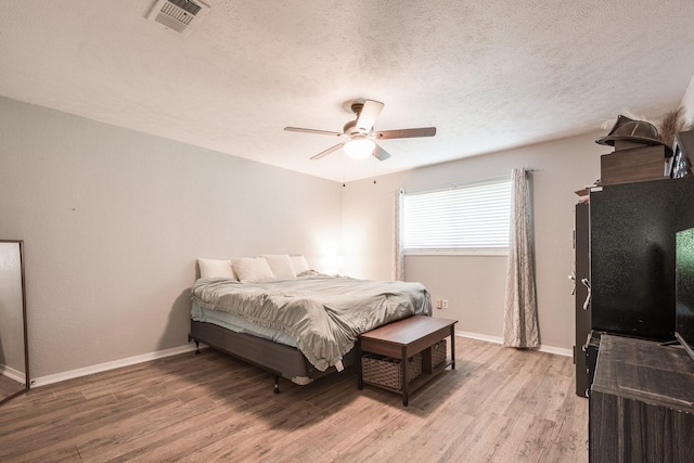 bedroom with a textured ceiling, visible vents, light wood finished floors, a ceiling fan, and baseboards