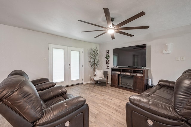 living area with light wood-type flooring, a fireplace, french doors, and ceiling fan