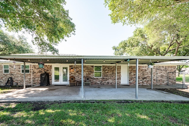 back of property with a yard, brick siding, a patio, and french doors