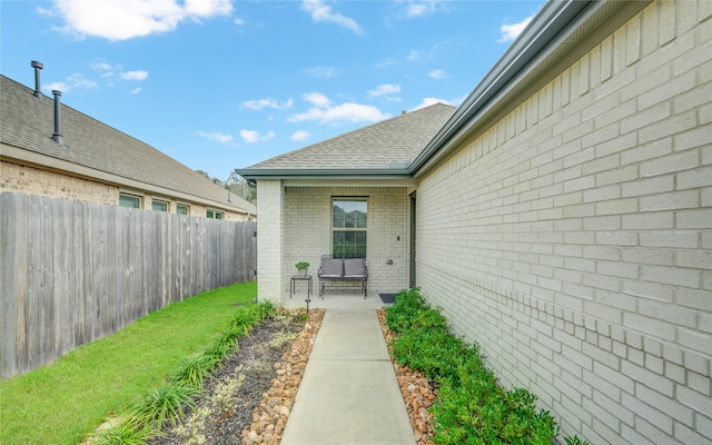 property entrance with a shingled roof, brick siding, fence, and a patio area
