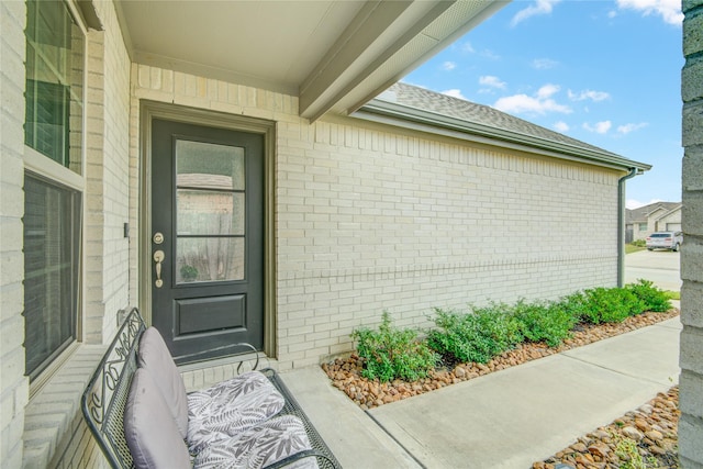 entrance to property featuring brick siding and roof with shingles