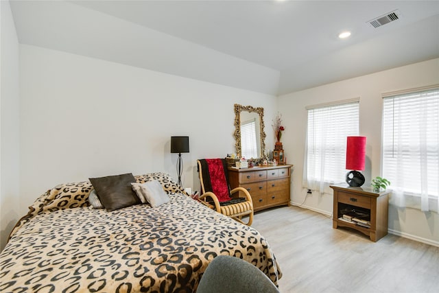 bedroom with light wood-style floors, visible vents, baseboards, and lofted ceiling