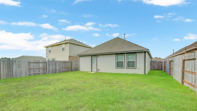 rear view of house with a fenced backyard, roof with shingles, and a yard