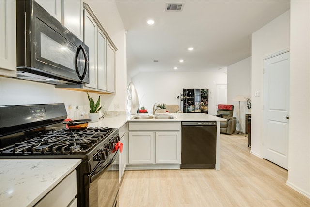 kitchen featuring a sink, a peninsula, light wood-type flooring, black appliances, and visible vents