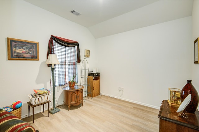 living area featuring vaulted ceiling, light wood-type flooring, visible vents, and baseboards