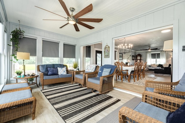 living room featuring a decorative wall, light wood finished floors, ornamental molding, and ceiling fan with notable chandelier