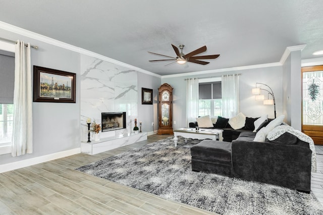 living area with wood finished floors, crown molding, baseboards, ceiling fan, and a high end fireplace