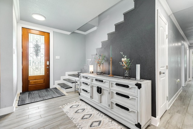 entrance foyer featuring light wood-type flooring, baseboards, ornamental molding, and stairs