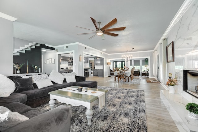 living area with baseboards, light wood finished floors, crown molding, and ceiling fan with notable chandelier