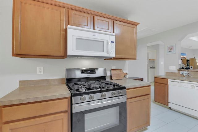 kitchen with washer / clothes dryer, white appliances, arched walkways, light countertops, and light tile patterned floors