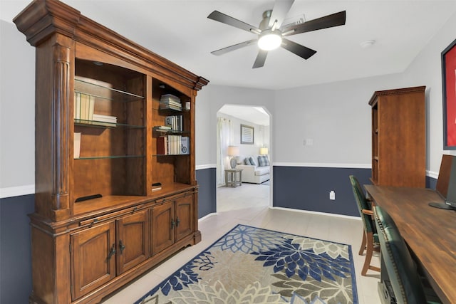 office area featuring light tile patterned floors, baseboards, ceiling fan, and arched walkways