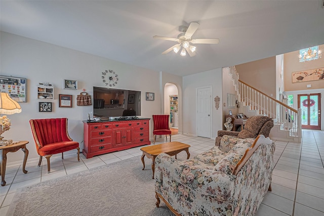 living area with light tile patterned floors, arched walkways, stairway, a ceiling fan, and baseboards
