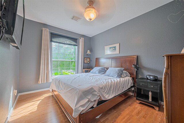 bedroom featuring wood finished floors, baseboards, vaulted ceiling, and a textured wall