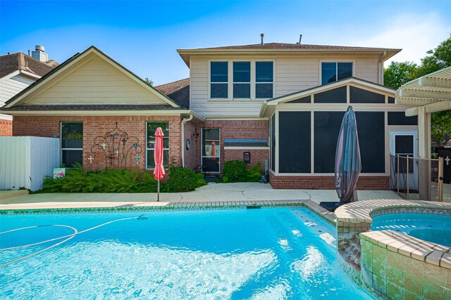 back of property with a sunroom, brick siding, a pool with connected hot tub, and fence