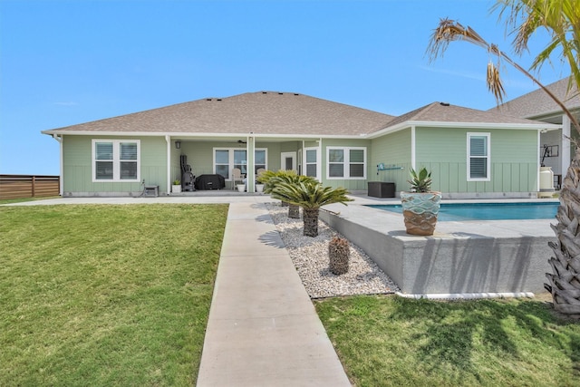 rear view of property with roof with shingles, board and batten siding, an outdoor pool, a patio, and a lawn