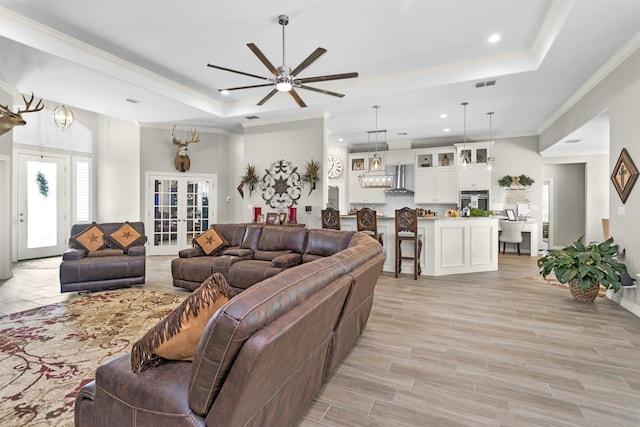 living area featuring light wood-style flooring, a ceiling fan, a tray ceiling, visible vents, and recessed lighting