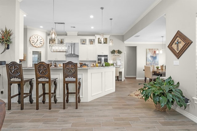 kitchen with light countertops, oven, white cabinetry, wall chimney range hood, and ornamental molding