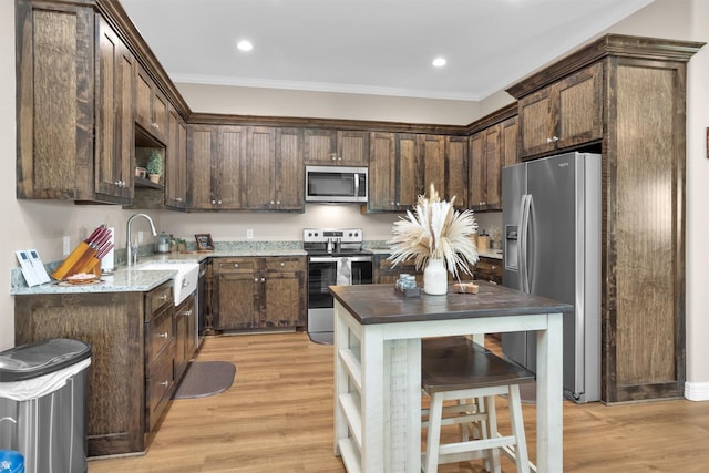 kitchen featuring a sink, appliances with stainless steel finishes, crown molding, dark brown cabinetry, and light wood-style floors