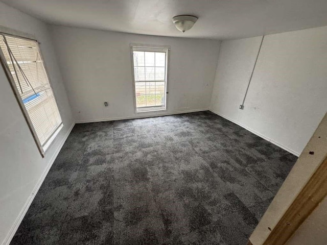 spare room featuring baseboards and dark carpet