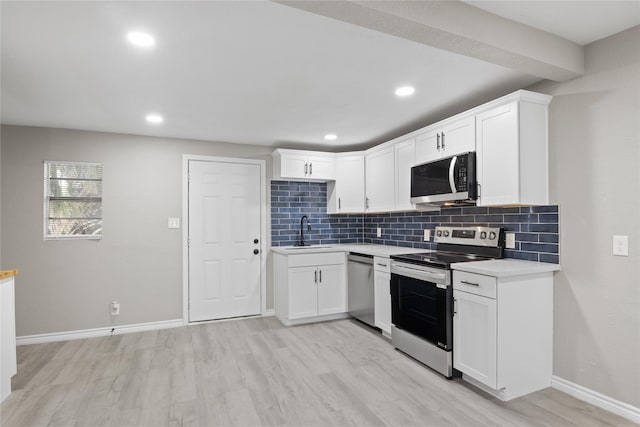 kitchen with a sink, appliances with stainless steel finishes, backsplash, light countertops, and light wood-style floors
