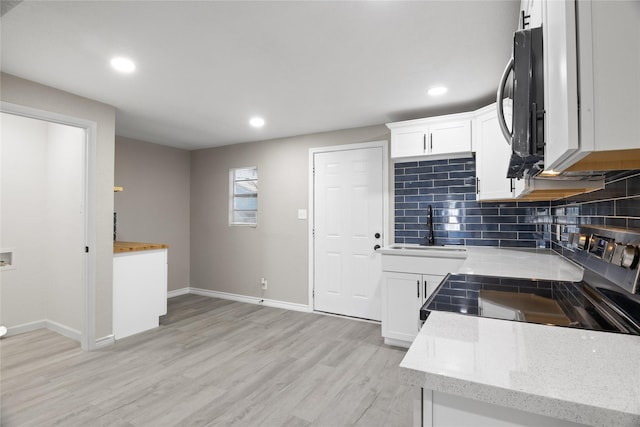 kitchen featuring a sink, light wood-type flooring, baseboards, decorative backsplash, and black microwave
