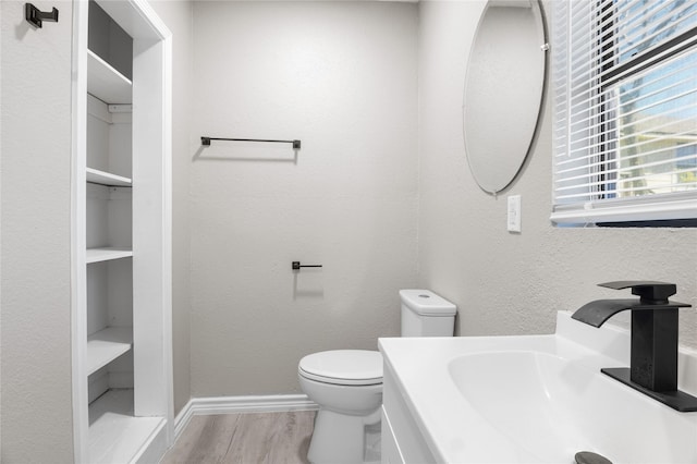 half bath featuring toilet, baseboards, a sink, and wood finished floors